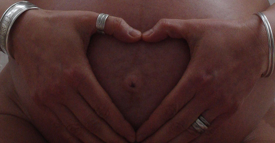 hands form a heart against a pregnant tummy